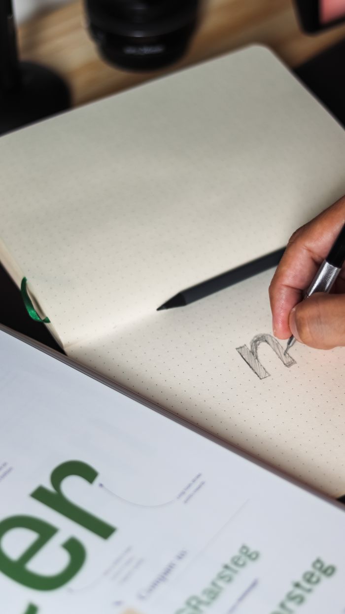 Une personne écrivant dans un carnet, concentrée sur le dessin au crayon et la conception typographique.